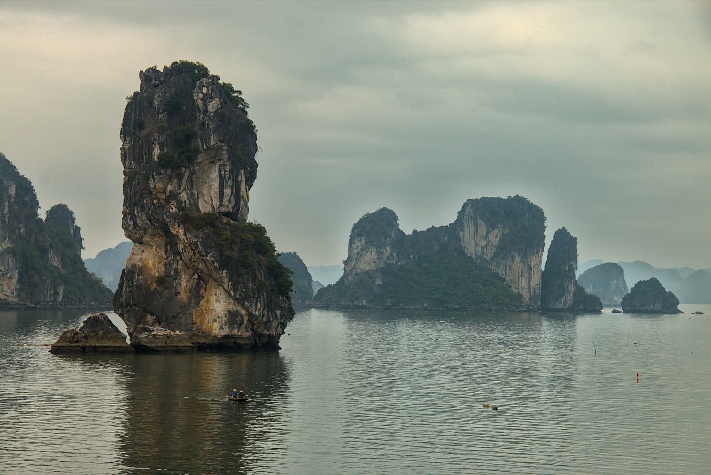 A tall limestone pillar and karst islands on calm water in Bai Tu Long Bay