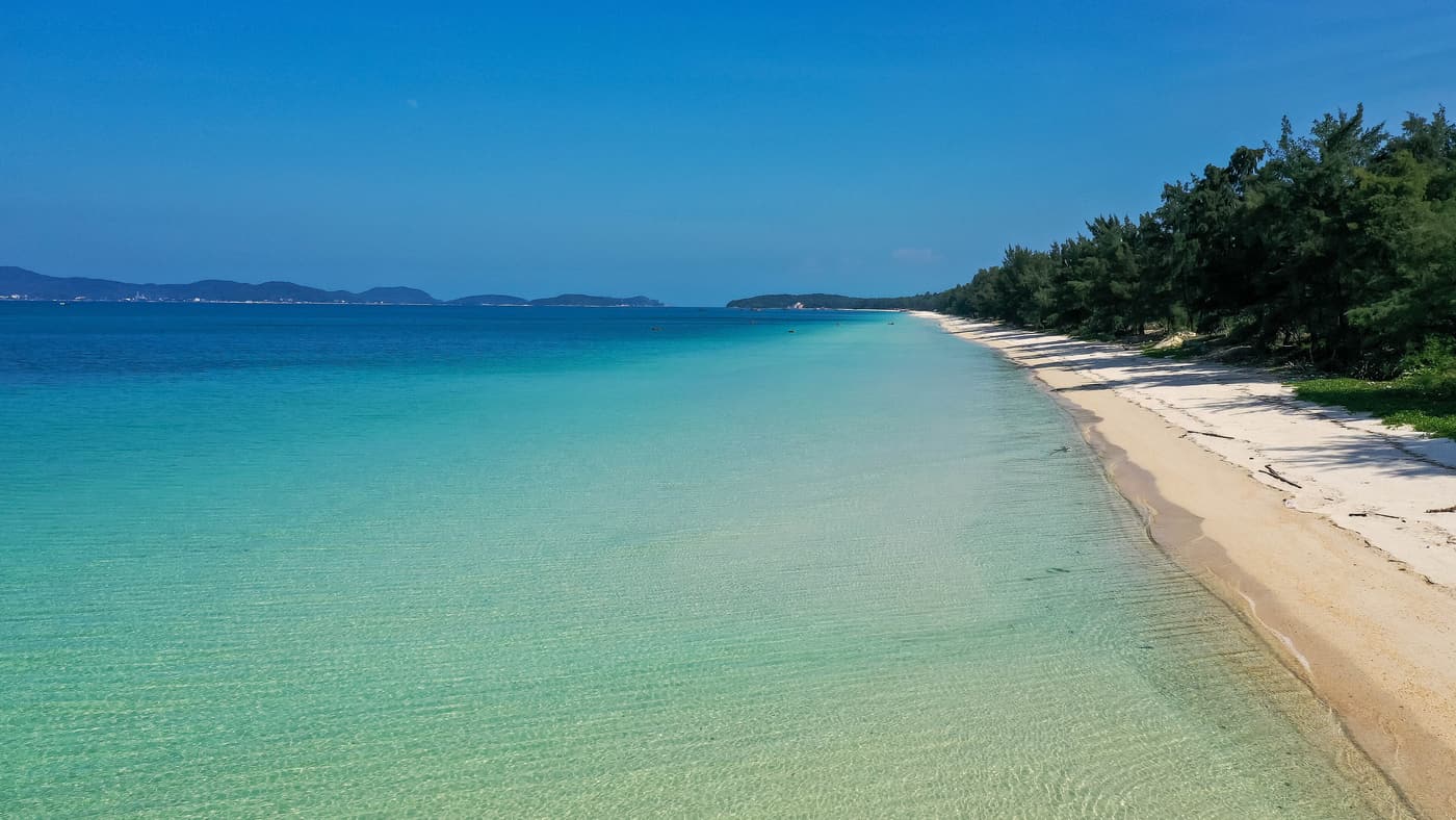 Turquoise water and a long pine-backed beach at Hong Van on Co To island
