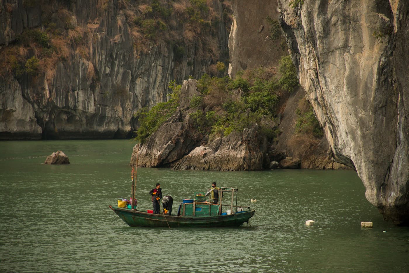 A small fishing boat beneath sheer limestone cliffs in Bai Tu Long Bay