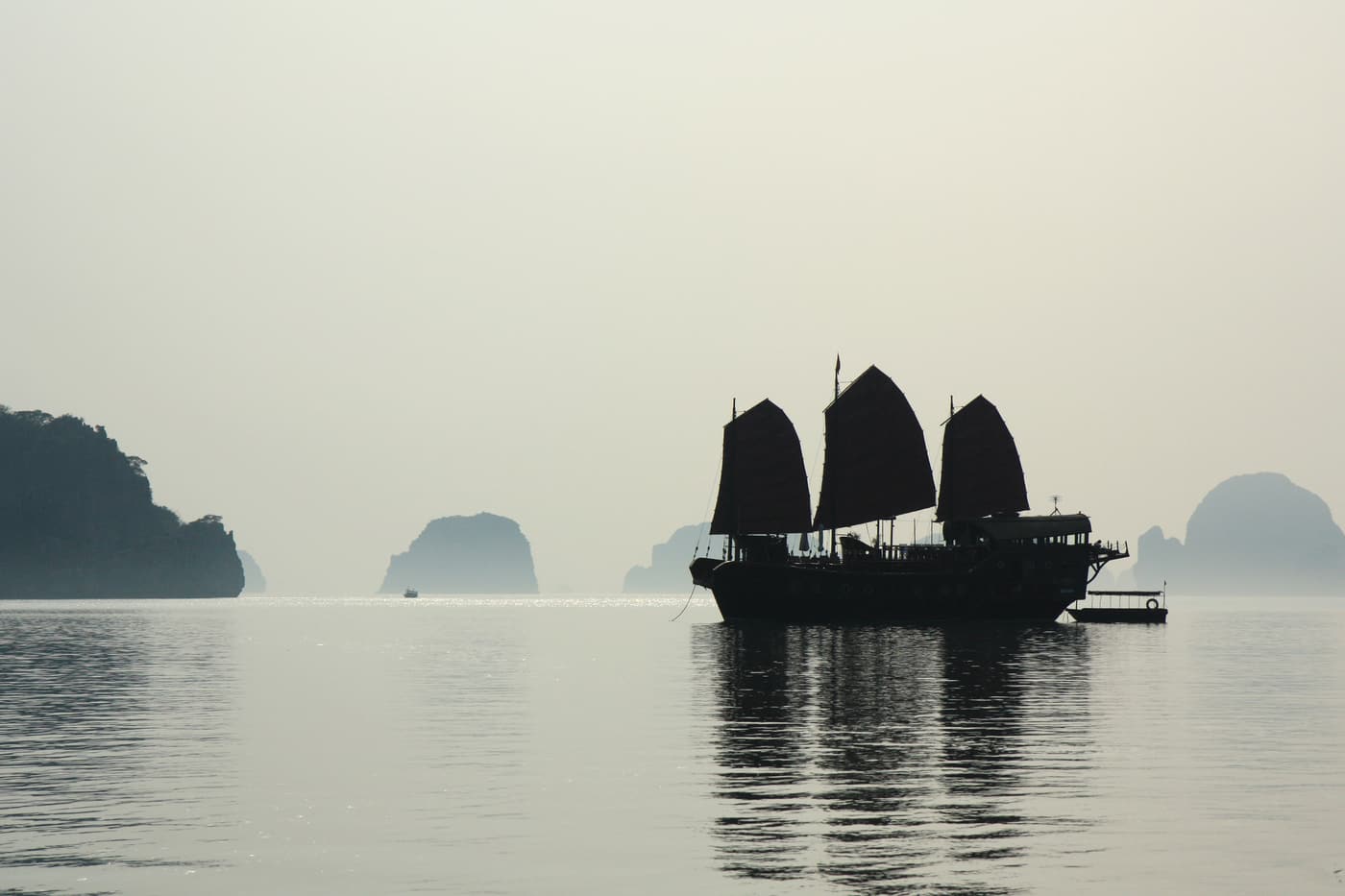 A junk silhouetted against misty karsts at dawn
