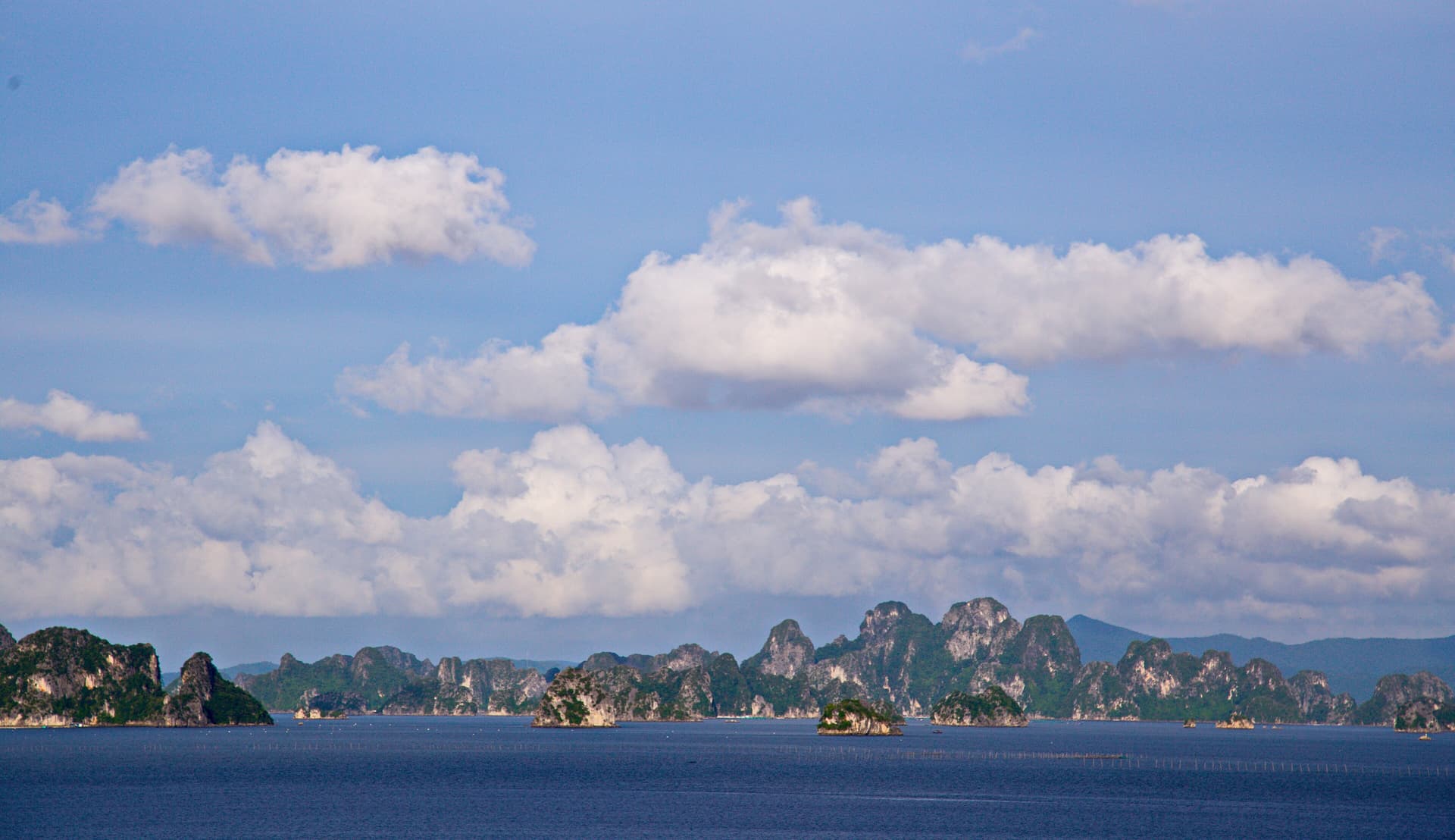 Limestone karst islands stretching across Bai Tu Long Bay under a blue sky