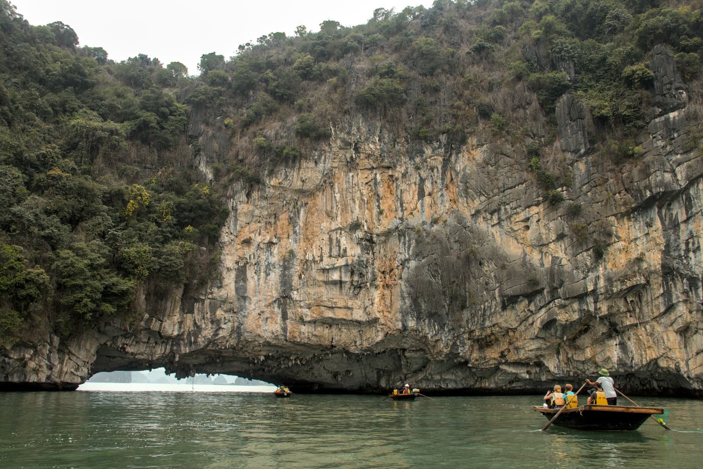 Rowing boats passing a natural rock arch in Bai Tu Long Bay